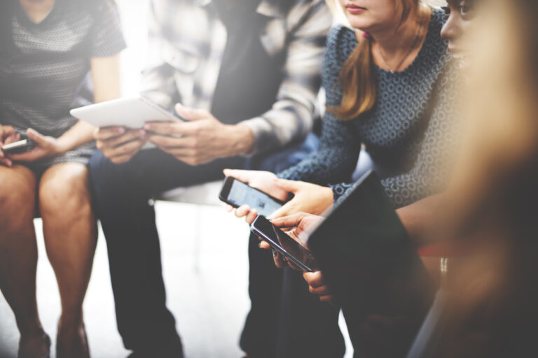 Group of colleagues sitting together using smartphones and tablets