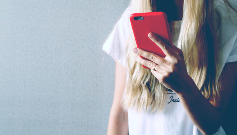 Woman holding a red smartphone, typing a text message