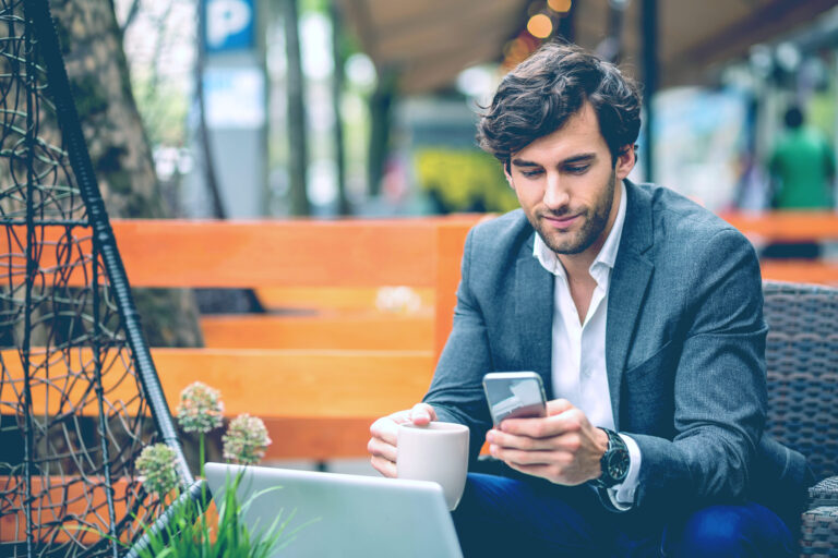 Businessman checking his phone at an outdoor café table with a laptop