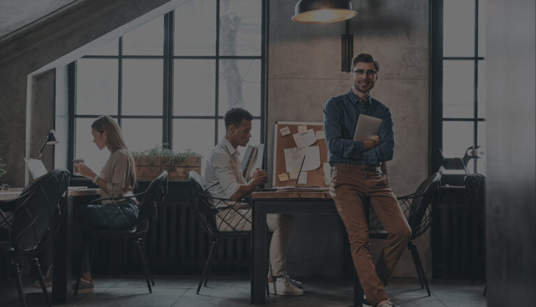Small team working in a modern loft office, one man standing with a laptop