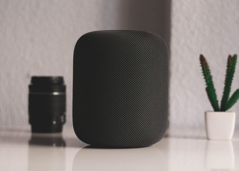 Smart speaker on a table next to a camera lens and a small cactus