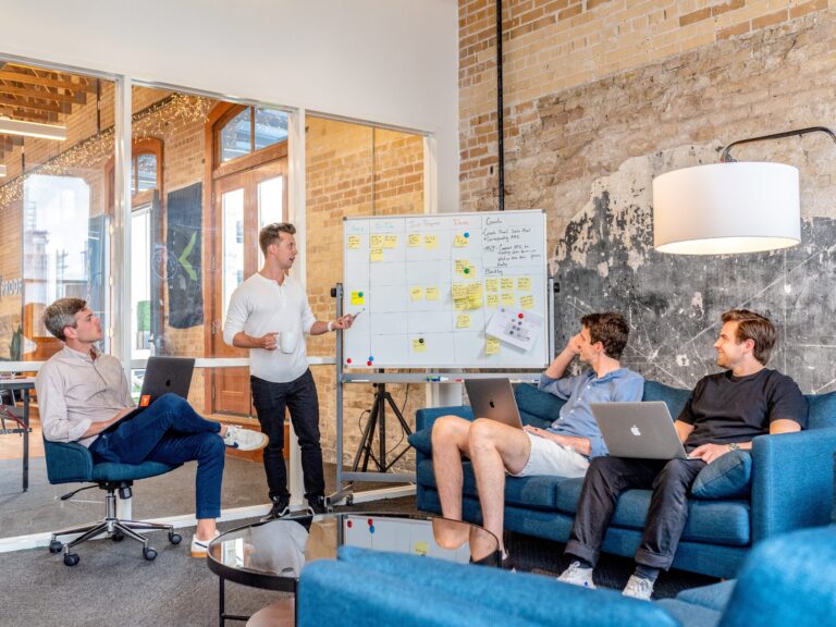 Team meeting around a whiteboard covered in sticky notes in a brick-walled office