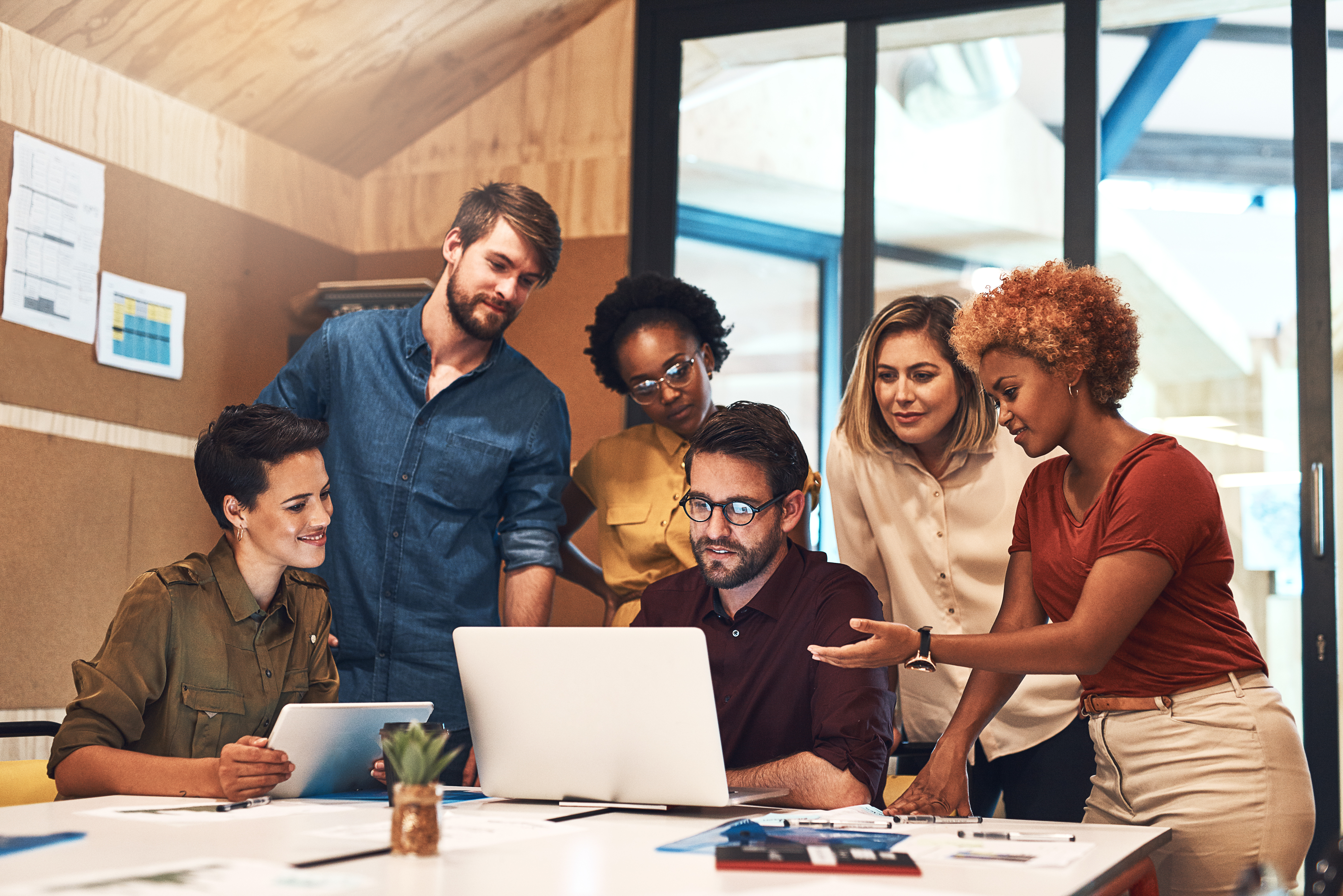 Diverse team gathered around a laptop and tablet in an office