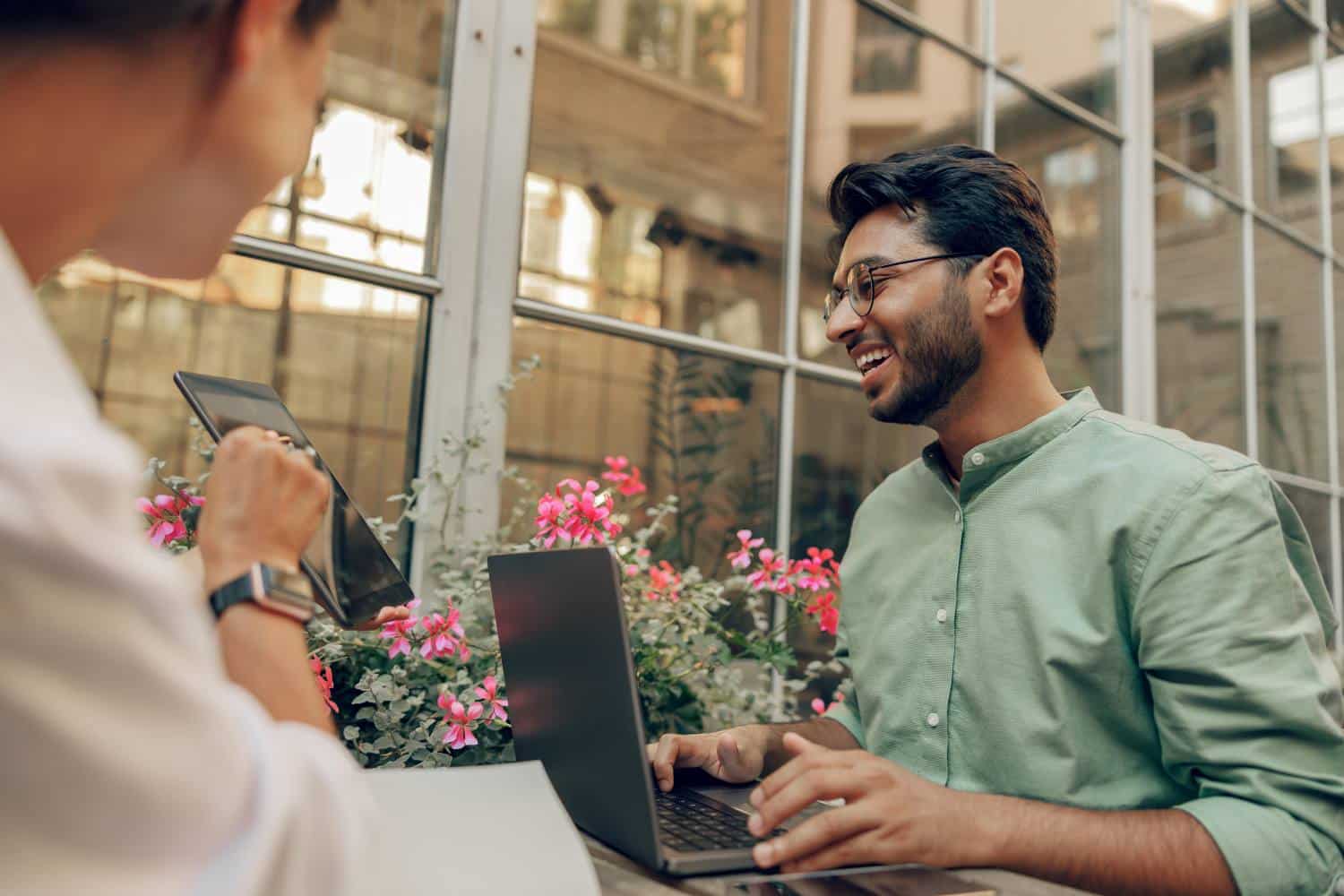 Smiling business colleagues discuss biz issue while use laptop sitting in office terrace