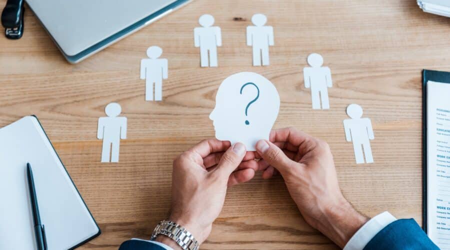cropped view of recruiter holding paper human shape with question mark on table
