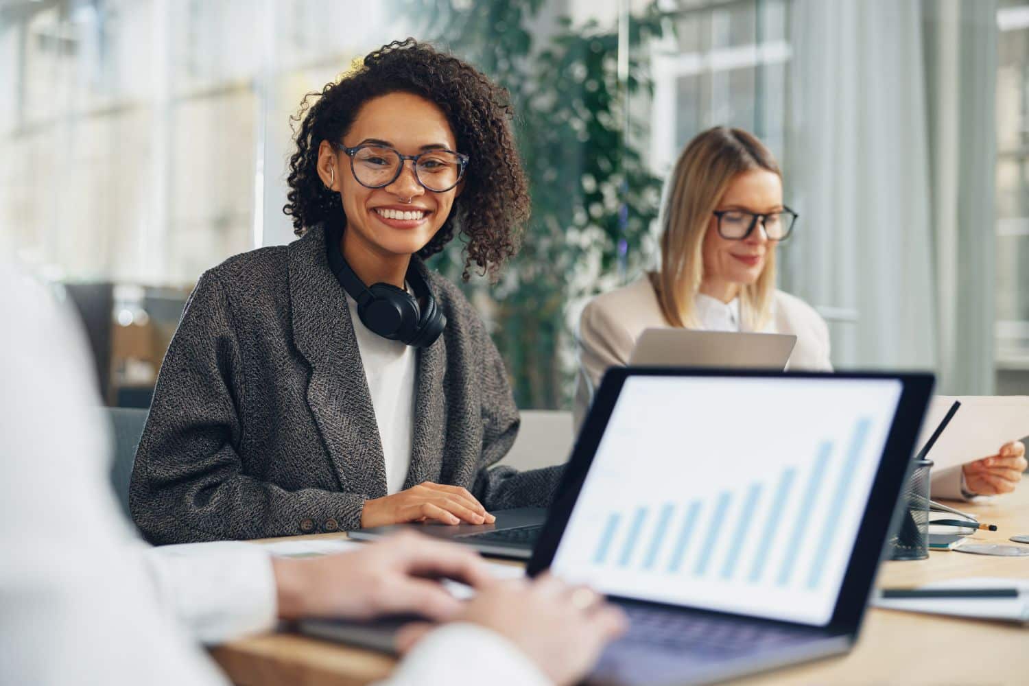 Smiling woman manager working on laptop in modern coworking while sitting near colleagues