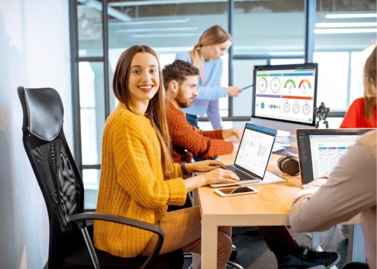 Smiling woman at a desk while colleagues work on Tracker dashboards